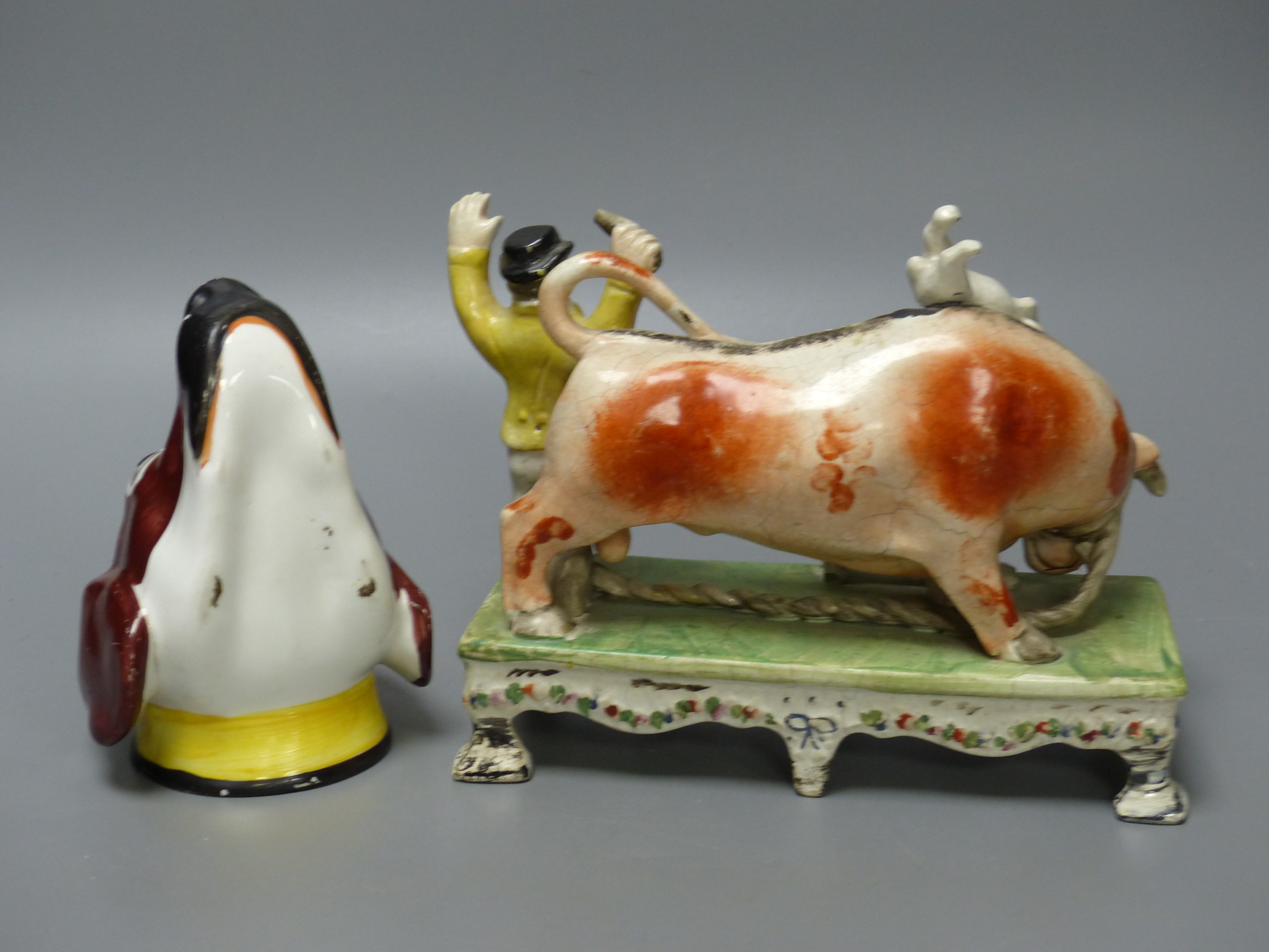 A 19th century Staffordshire bull baiting group, width 19cm, and a 19th century English porcelain spaniel’s head stirrup cup (2)